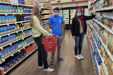 Burroughs junior Emma Kimbler, senior ZJ Hoffman, and junior Mahnoor Ahmad stock up on canned goods for their CSF food drive. 