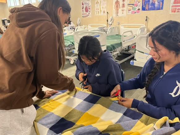 Junior Abigail Esparza, Sophomore Cynthia Bimbela, and Keyla Pimentel carefully cut strips of fleece from the edges to put together a blanket. 