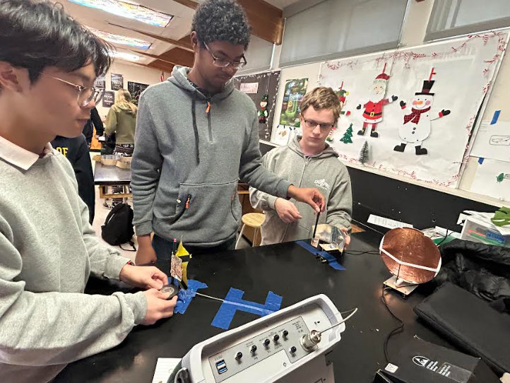 Junior Alex Tuey, senior Elishua Flowers, and senior Andrew Savini experiment with aluminum-covered surfaces to transfer a signal between a transmitter and receiver, mirroring how real-world cell towers transmit data.